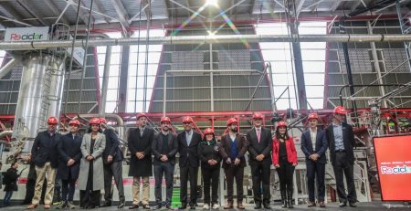 Grupo de personas con cascos rojos en una planta de reciclaje de botellas de plástico